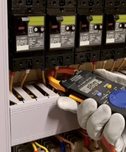 Electrician using HIOKI CM3289 True RMS clamp meter to measure motor current in industrial control panel