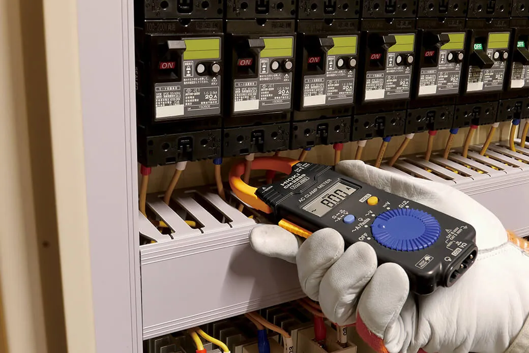Electrician using HIOKI CM3289 True RMS clamp meter to measure motor current in industrial control panel